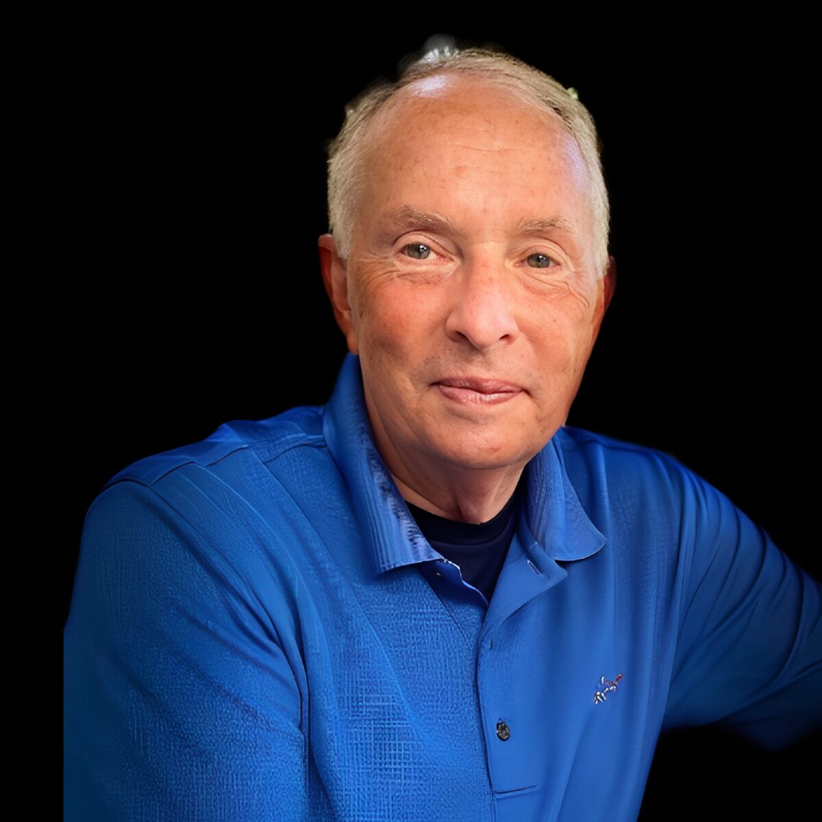 Elderly man wearing a blue shirt, smiling.
